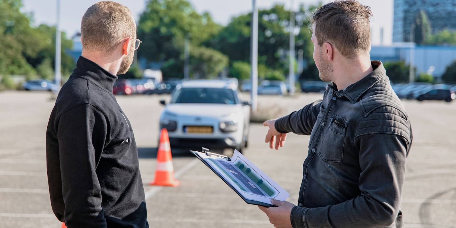 Two people discussing a used car on a lot, one pointing while holding a clipboard